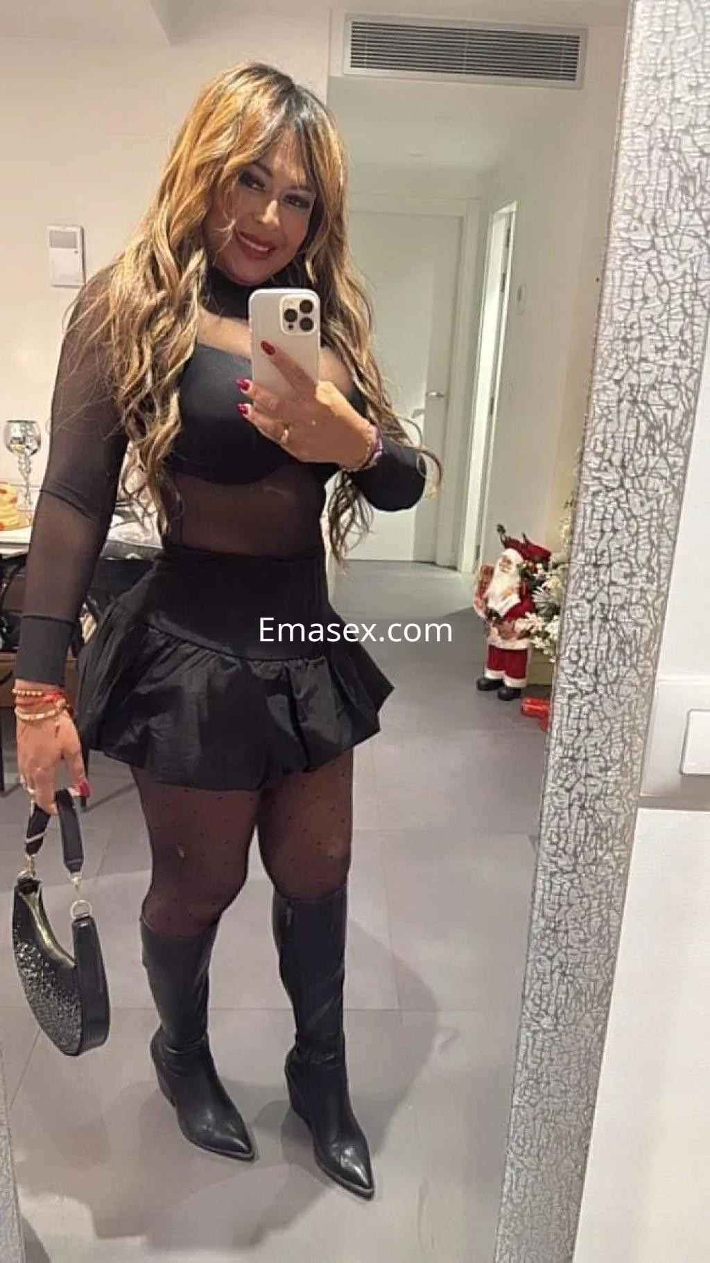 La puta posando frente al espejo en Murcia, viste una blusa transparente y una falda corta negra.