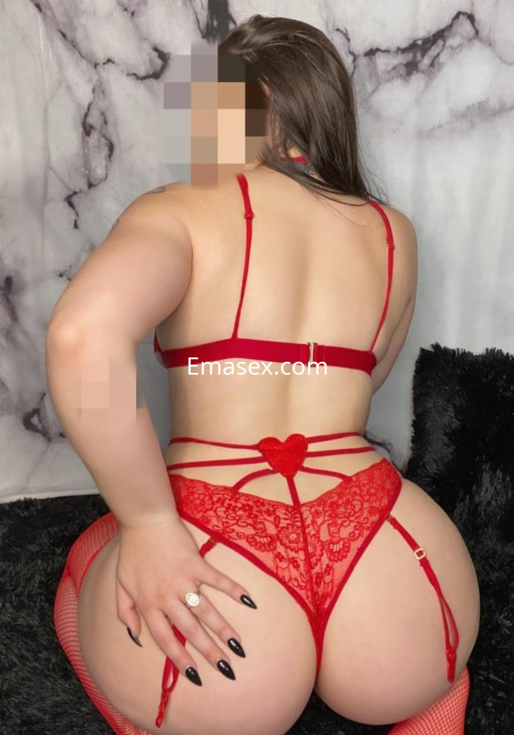 Escort en Pamplona con lencería roja, posando de espaldas sobre un fondo gris y negro, mostrando detalles de encaje.