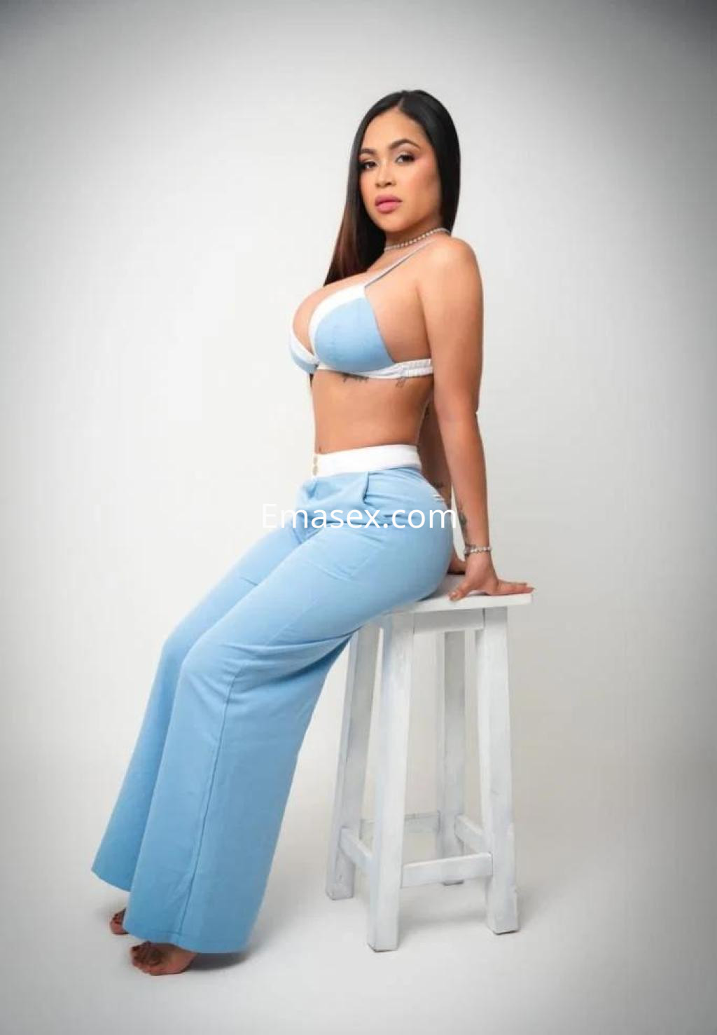 Escort en Tenerife sentada sobre un taburete, luciendo un conjunto de dos piezas azul claro y con cabello largo.