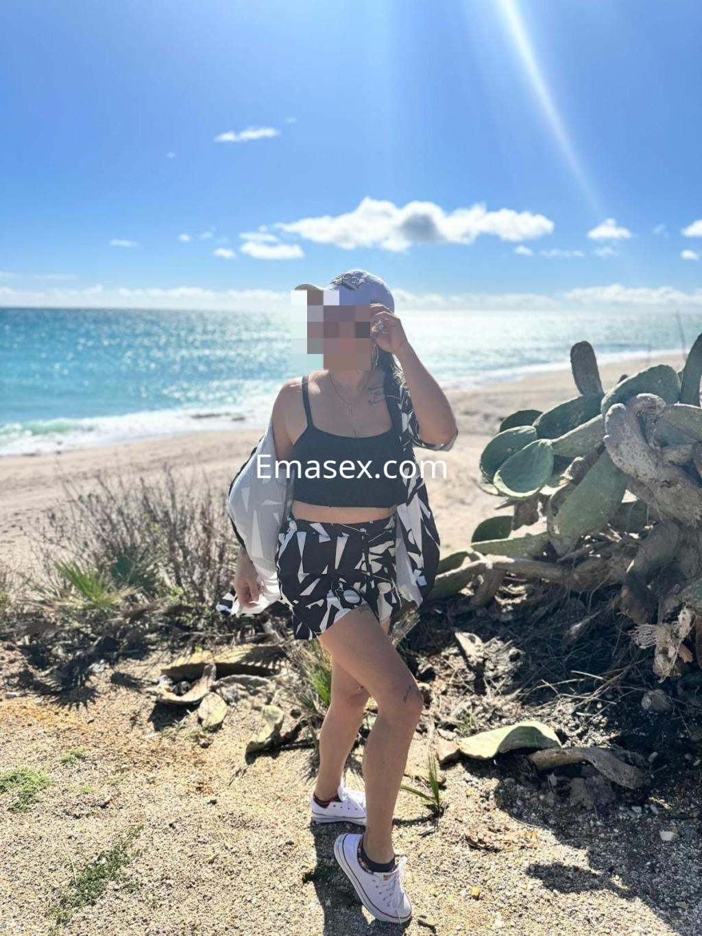 Escort caminando por la playa en Valencia, luciendo un conjunto de top negro y falda corta con estampado.