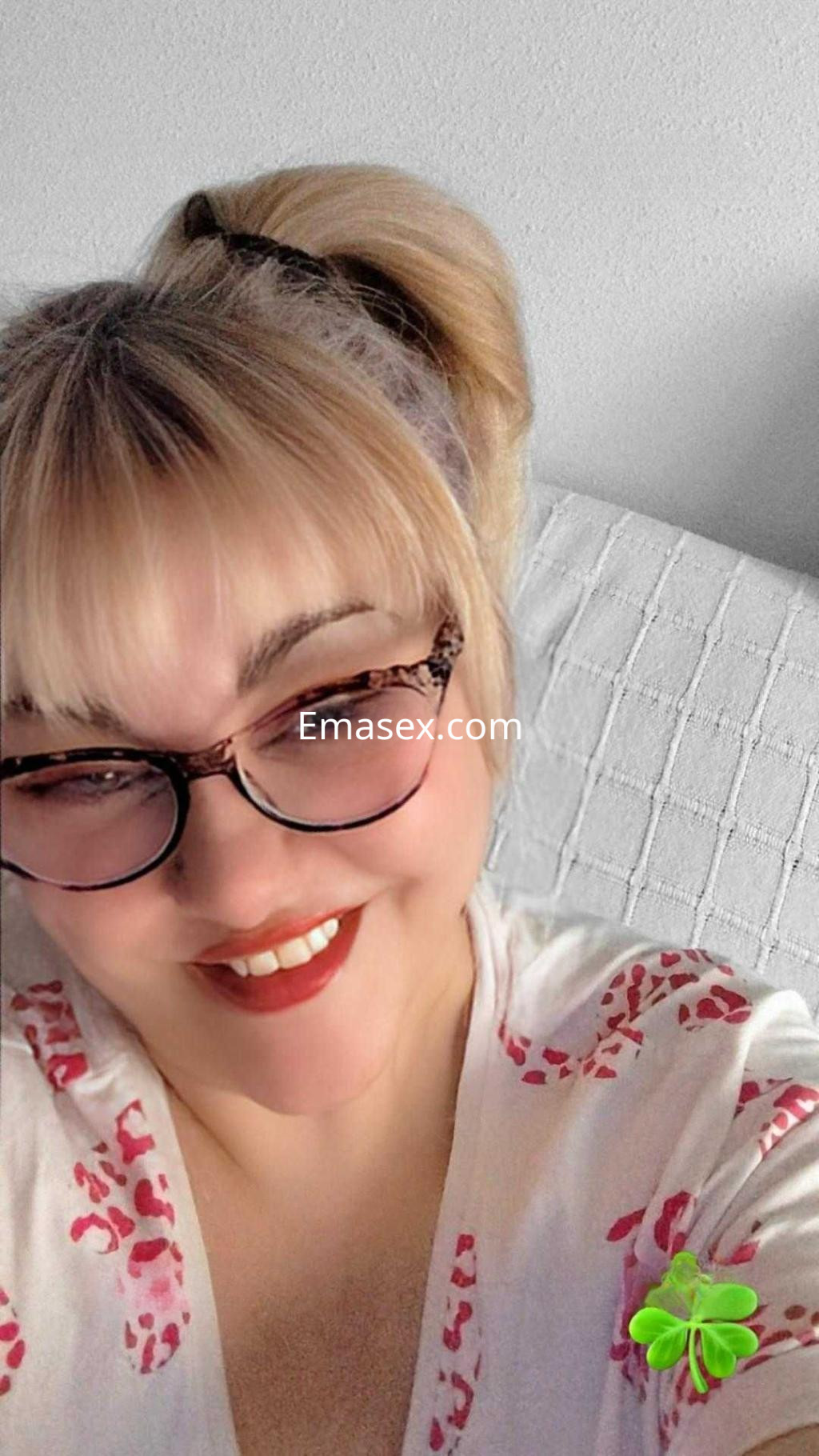 Escort en Valladolid con cabello rubio recogido, usando gafas y una camiseta con estampado animal, sonriendo.