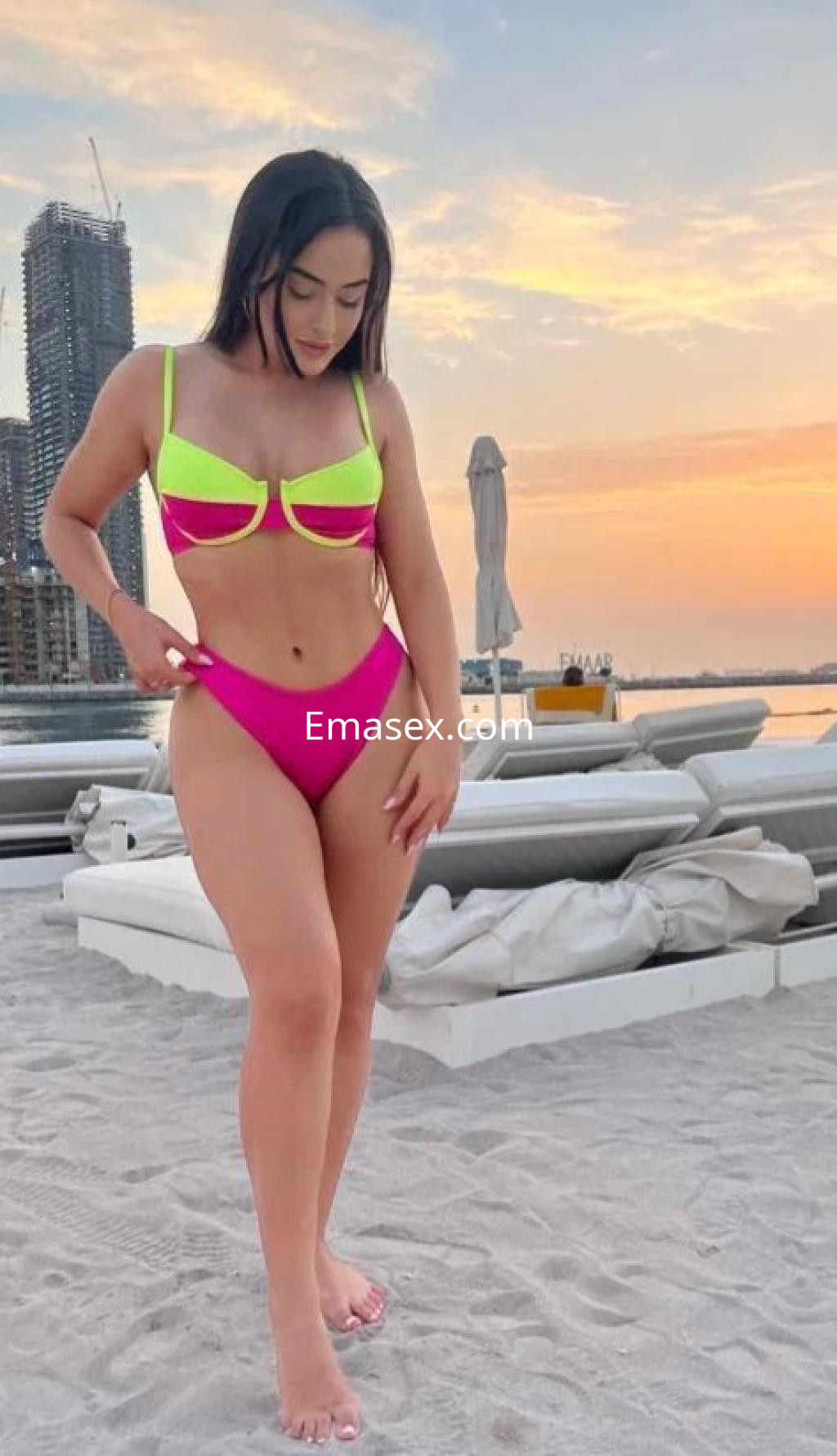Puta en Palma de Mallorca, luciendo un bikini neón rosa y amarillo, de pie junto a una playa al atardecer.