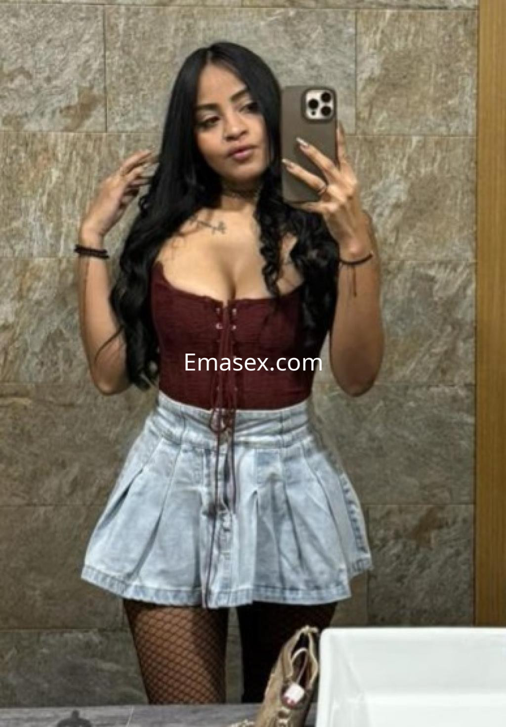 Escort en Castellón con cabello largo y oscuro, luciendo un corset burdeos y una falda corta de mezclilla.