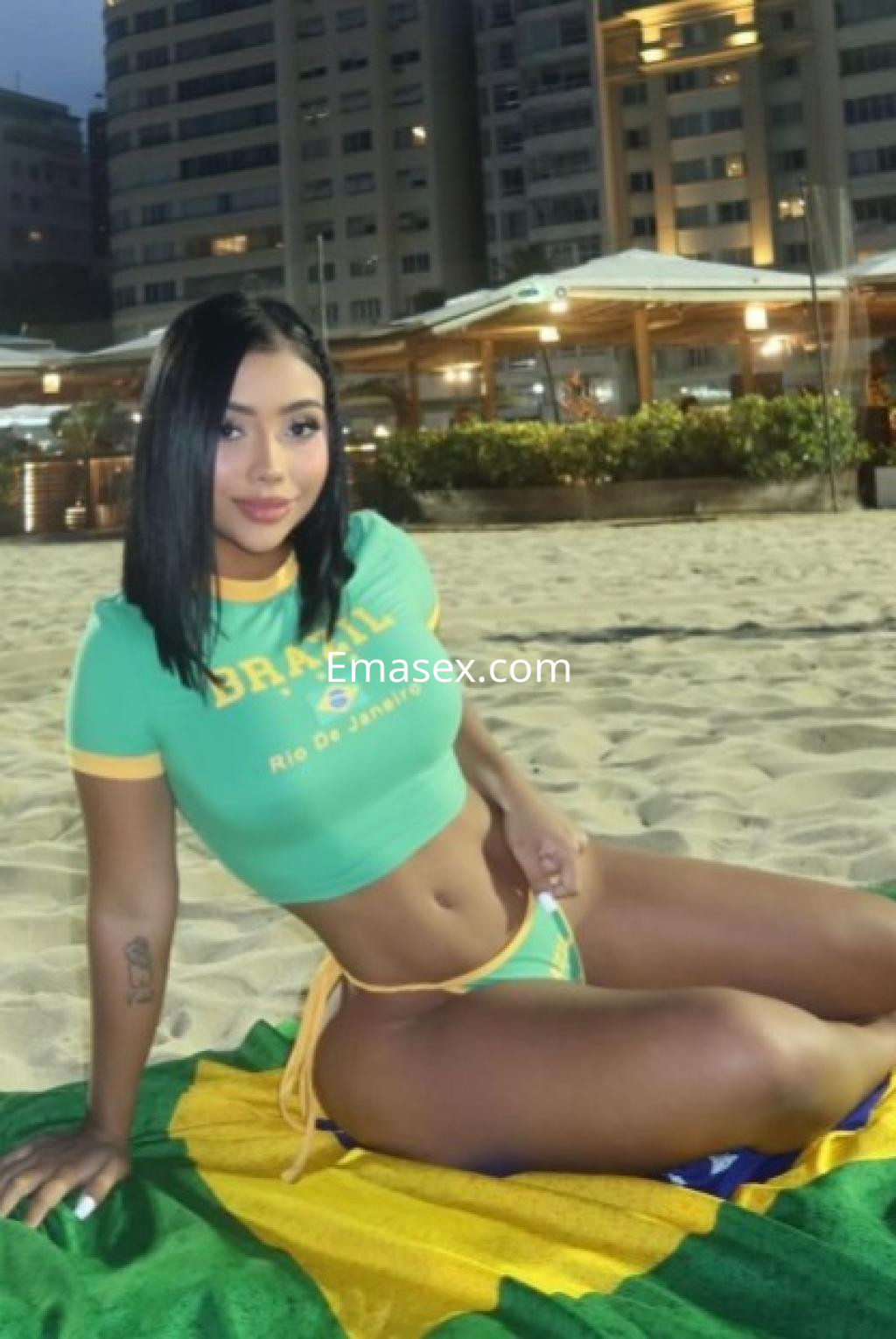 Escort en Tenerife posando en la playa con un top verde y bikini, luciendo un cabello oscuro y lacio.