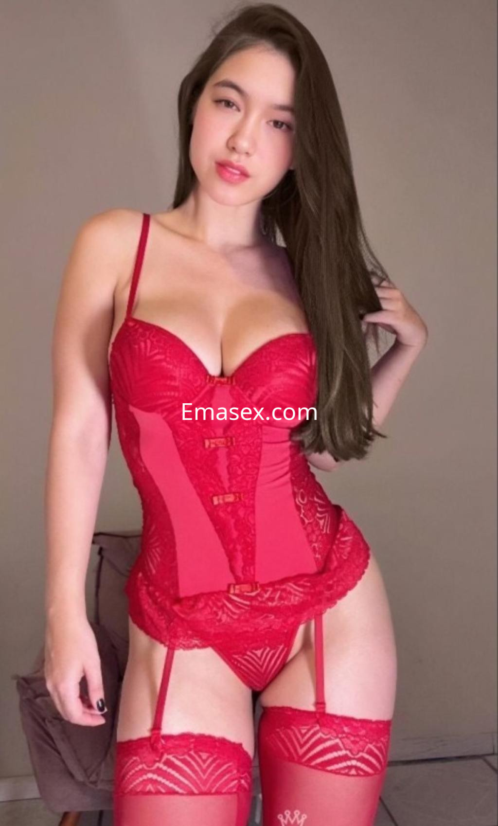 Escort en Vitoria luciendo un corsé rojo y medias a juego, con cabello largo y lacio, en un fondo neutro.