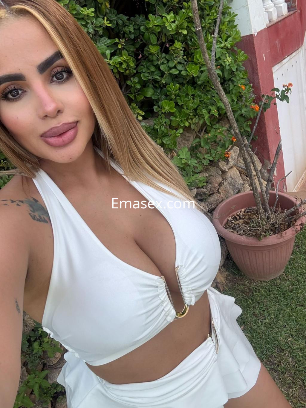 La puta posa con un vestido blanco en un entorno natural, mostrando su cabello largo y rubio.