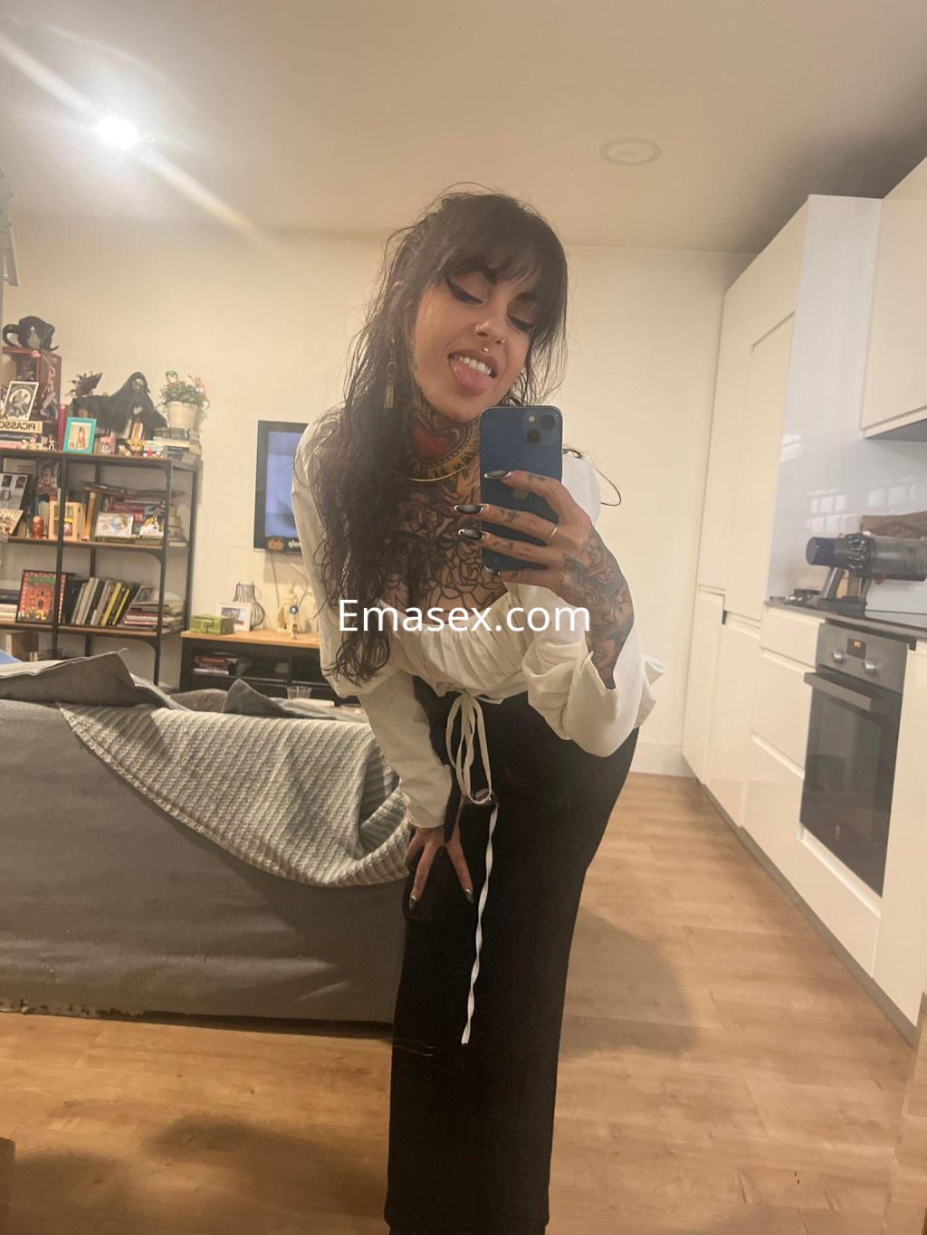 La puta en Zaragoza posa en un espejo, luciendo un top blanco y pantalones oscuros, con cabello rizado.
