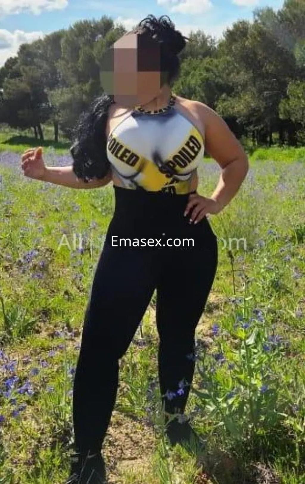 Escort en Albacete posando en un campo con flores, lleva un top ajustado y leggins negros, cabello rizado.