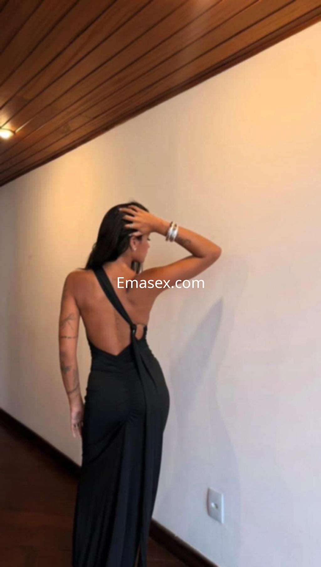 Escort en Alicante con un vestido negro de espalda descubierta, posando de perfil en un ambiente interior.