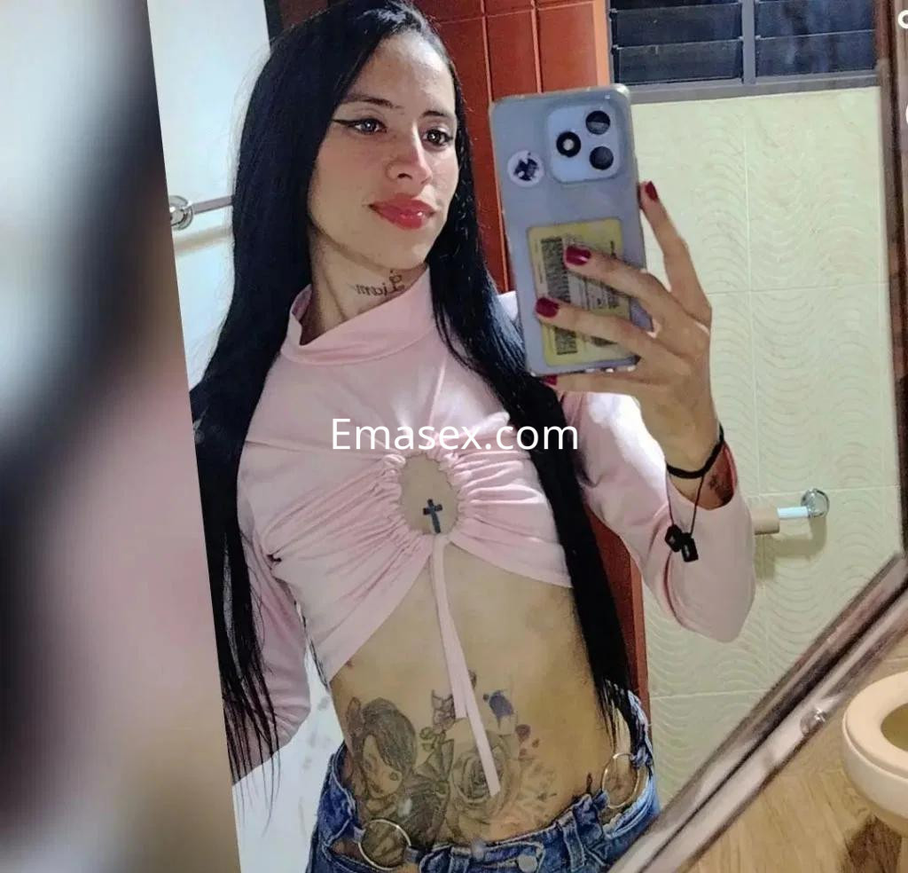 Puta en Badajoz con cabello largo y lacio, viste un top rosa ajustado y jeans, mostrando tatuajes en el abdomen.