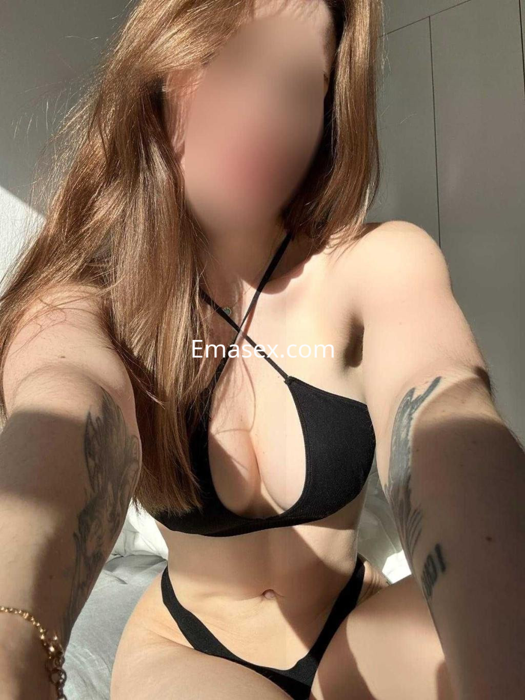 Puta con cabello largo y castaño, viste un bikini negro que resalta su figura en un ambiente iluminado en Badajoz.
