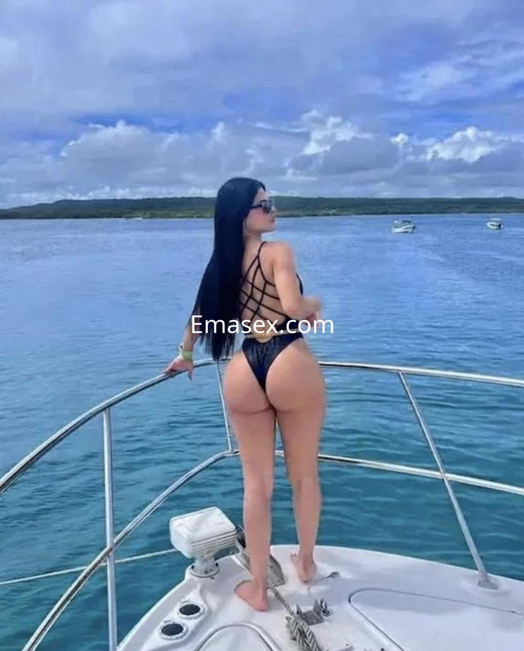Escort en Palma de Mallorca, de cabello negro y piel clara, posa de espaldas en un yate con un traje de baño negro.