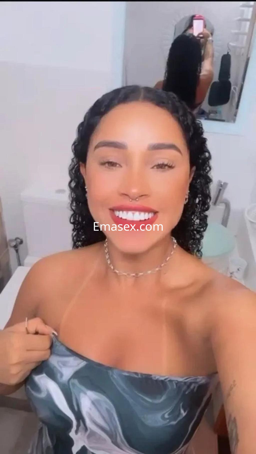 Puta con cabello rizado y oscuro, sonriente, en un baño con decoración moderna en Palma de Mallorca.