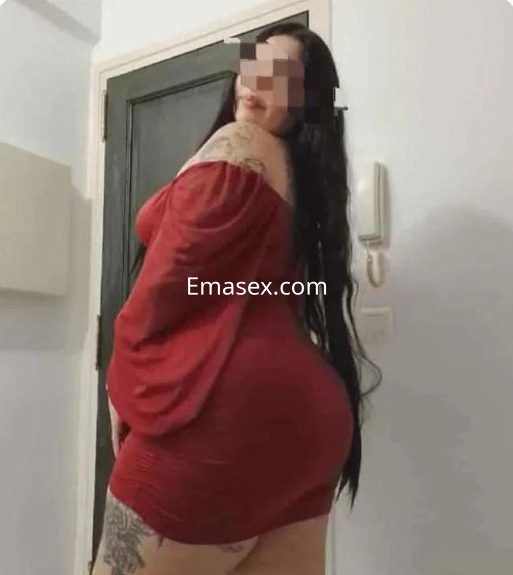 Escort en Barcelona, de cabello largo y oscuro, viste un vestido rojo ajustado y muestra un tatuaje en el brazo.