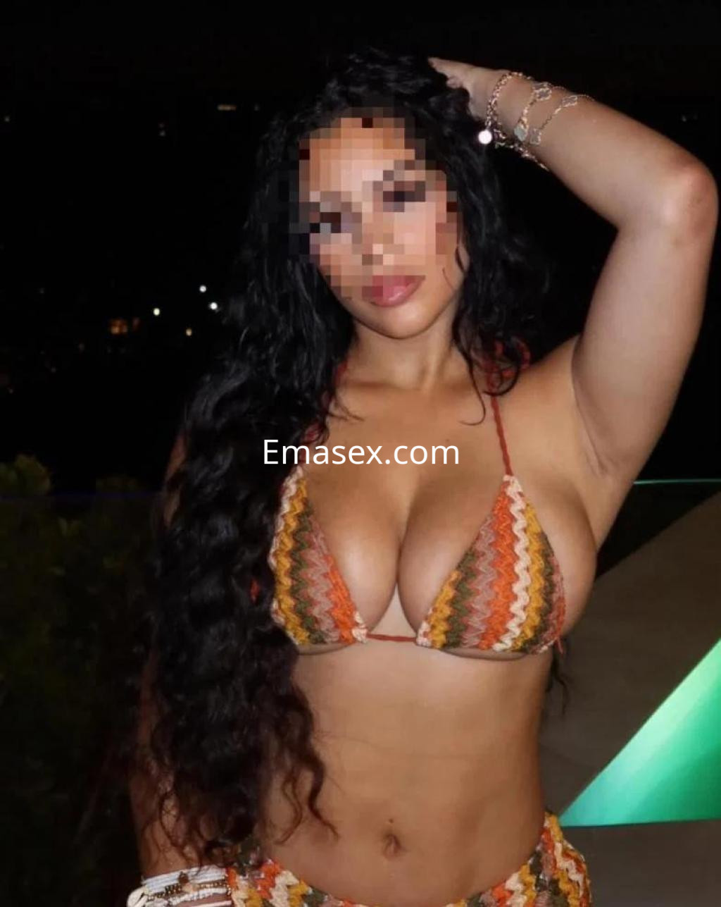 Escort en Barcelona con cabello largo y rizado, vistiendo un bikini de colores vibrantes y posando con una mano en la cabeza.