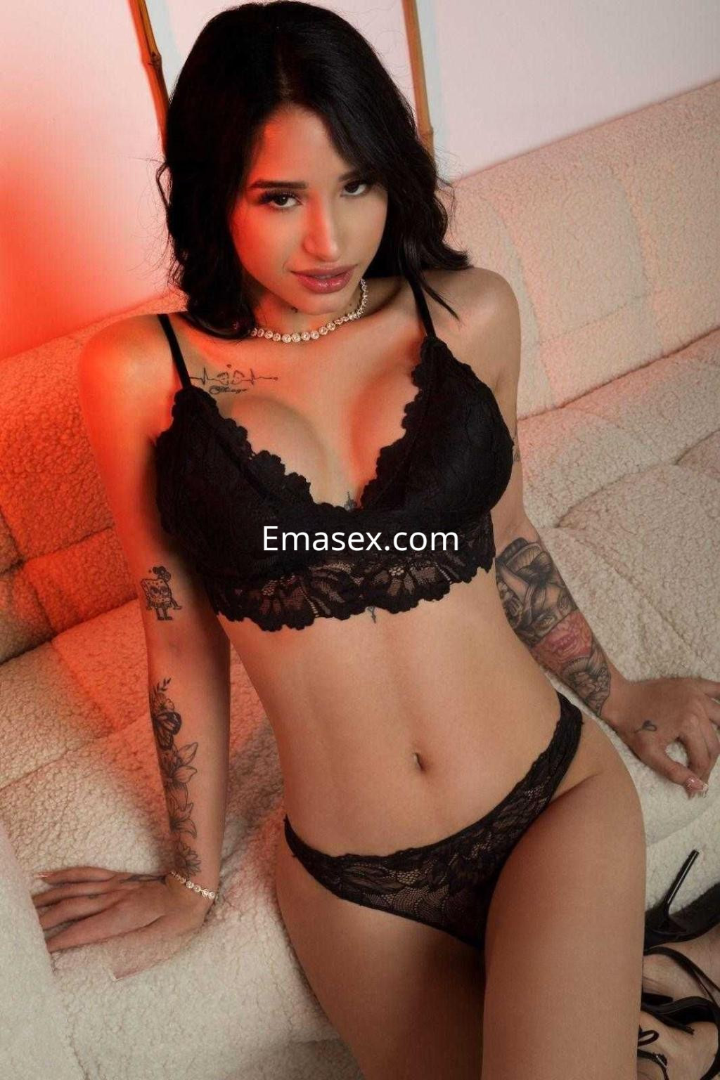 Escort en Barcelona con cabello oscuro y ondulado, vistiendo lencería negra de encaje en un entorno iluminado con luces suaves.