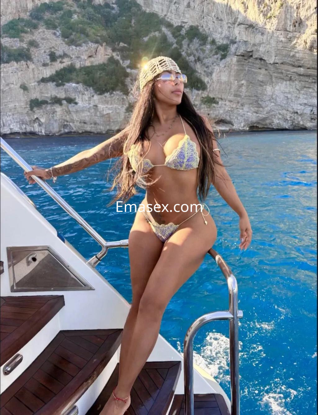 Puta posando en un yate en Burgos, luciendo un bikini colorido y gafas de sol, con el mar de fondo.