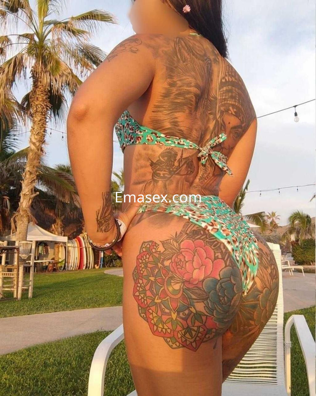 Escort en Cáceres con traje de baño de estampado colorido, mostrando sus tatuajes en un entorno al aire libre.