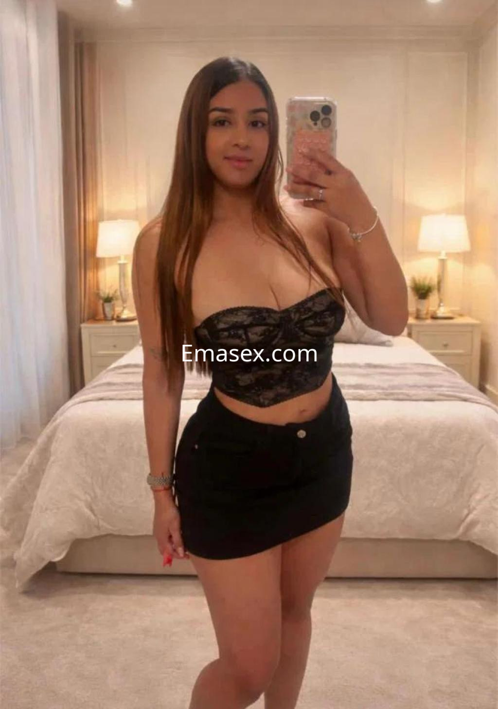 Escort en Castellón posando frente a un espejo, con top negro de encaje y falda corta, en un ambiente acogedor.