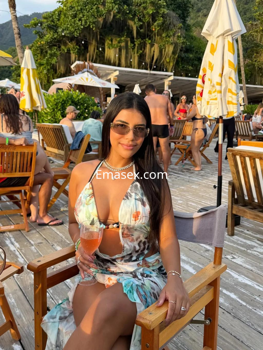 Puta con vestido floral y gafas de sol, sentada en una silla en un ambiente al aire libre en Coruña.