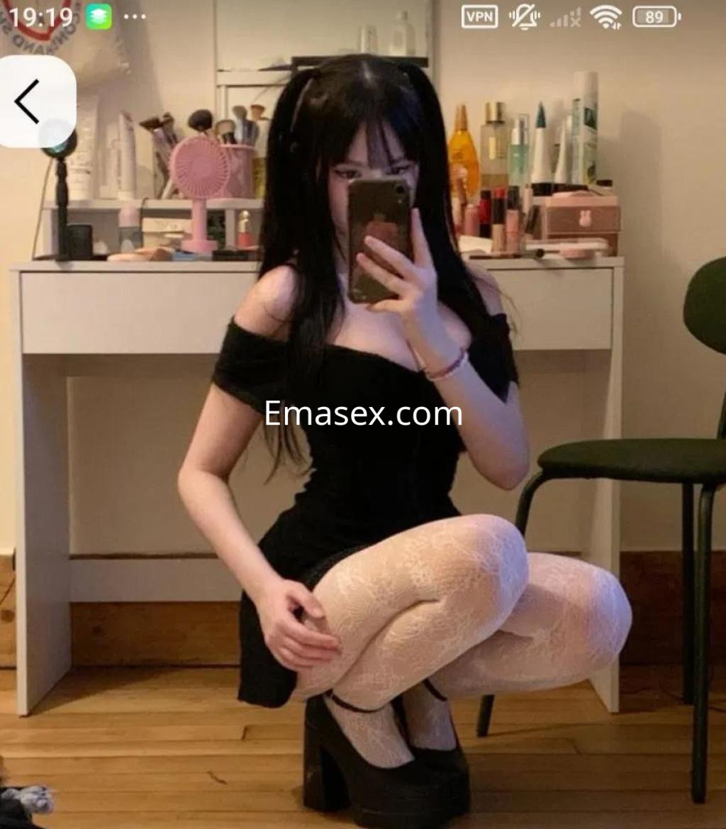 La puta en Coruña se muestra en un vestido negro ajustado, con medias blancas y tacones altos, posando frente a un espejo.