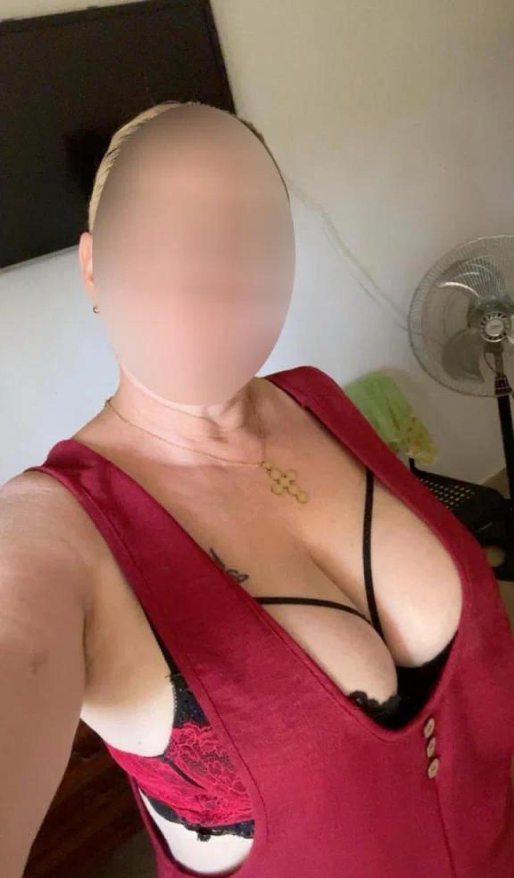 Puta en Murcia con cabello rubio, luciendo un vestido rojo que resalta su escote y lencería negra.