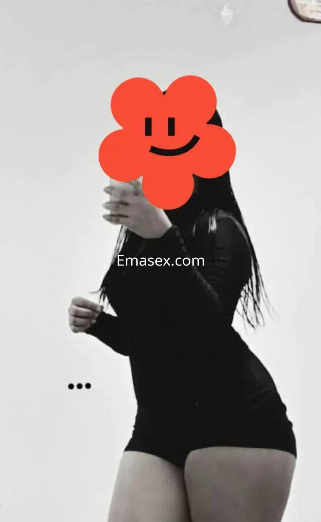 Puta posando de perfil en un ajustado body negro, con cabello largo y lacio, en un entorno minimalista en Murcia.