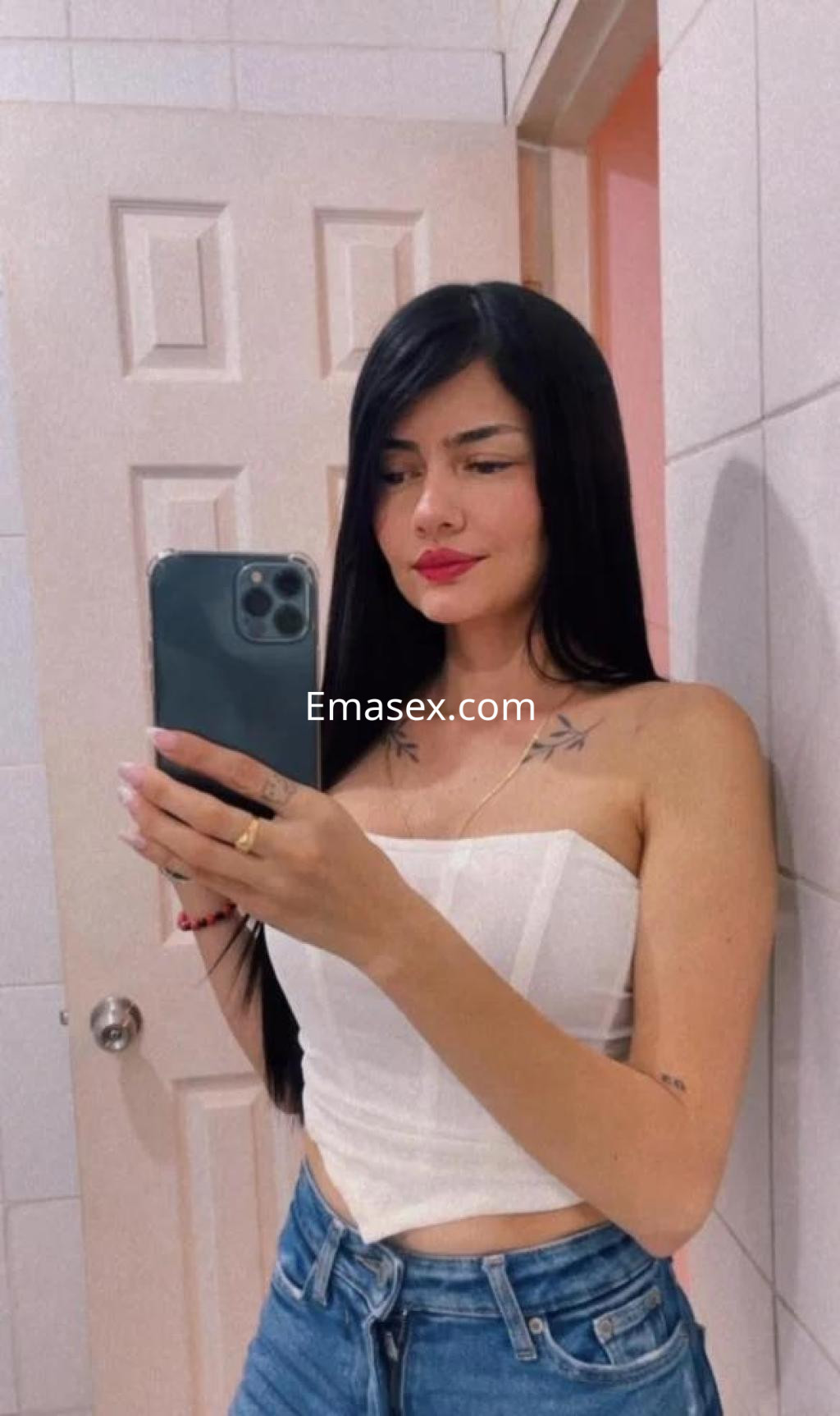 Escort en Murcia con cabello largo y lacio, viste una blusa blanca y jeans, posando frente a un espejo.