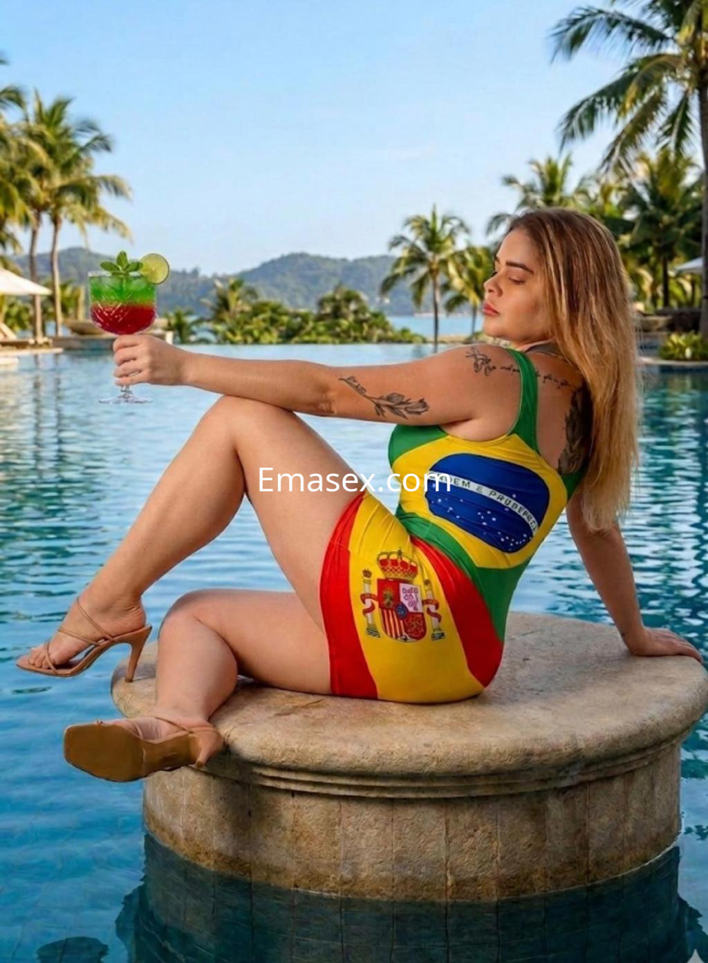 Escort en Pamplona luciendo un bañador con banderas, sentada en una piedra junto a la piscina, sosteniendo un cóctel.