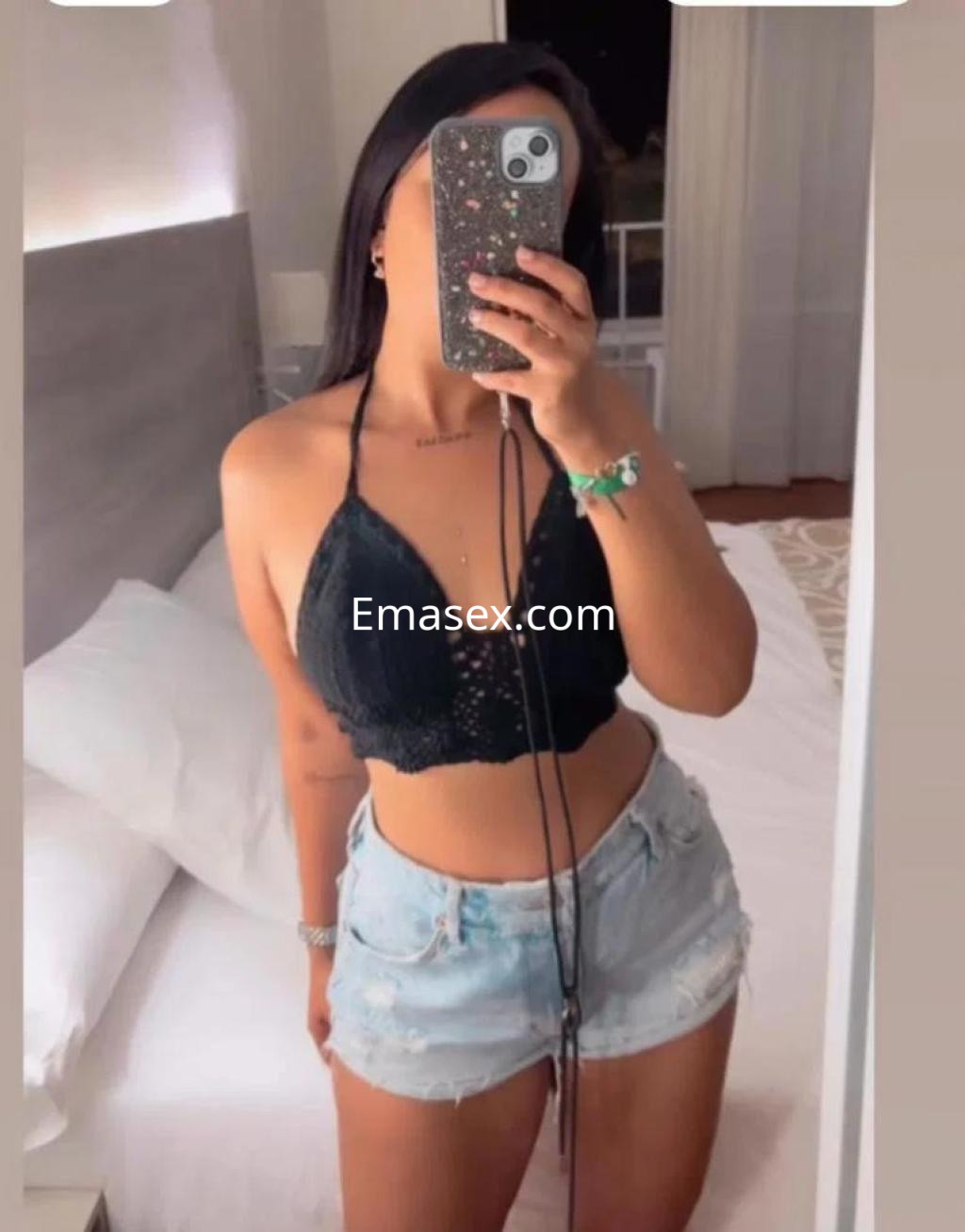 Escort en Las Palmas con top negro y shorts de mezclilla, posando frente a un espejo en un ambiente iluminado.