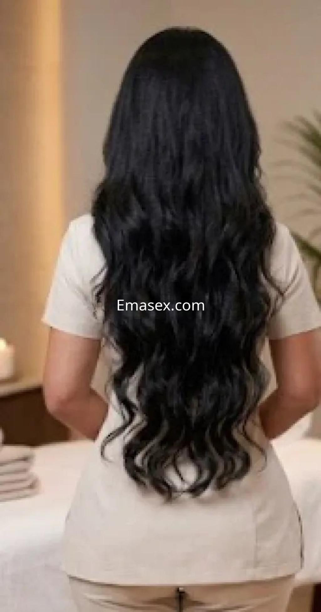 Escort de cabello largo y rizado, vista desde atrás, con atuendo claro en un ambiente elegante en Valencia.