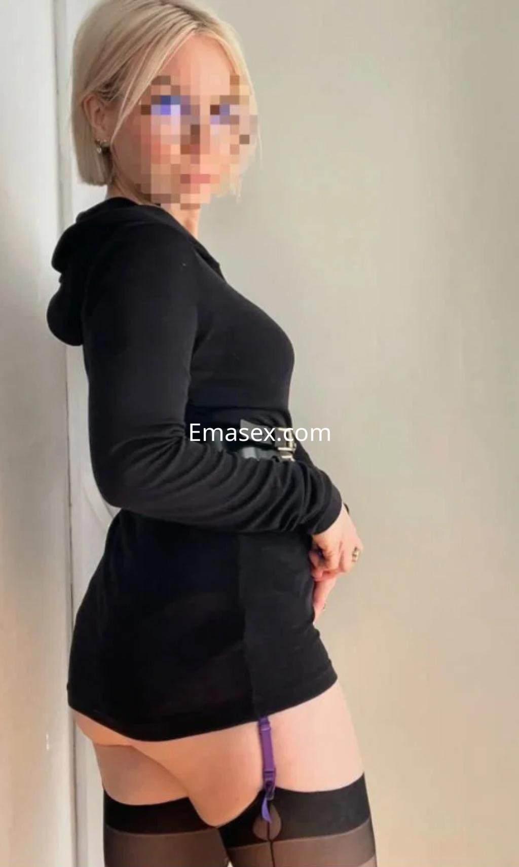 Escort en Burgos con pelo corto y rubio, vistiendo un vestido negro ajustado y medias con liga.