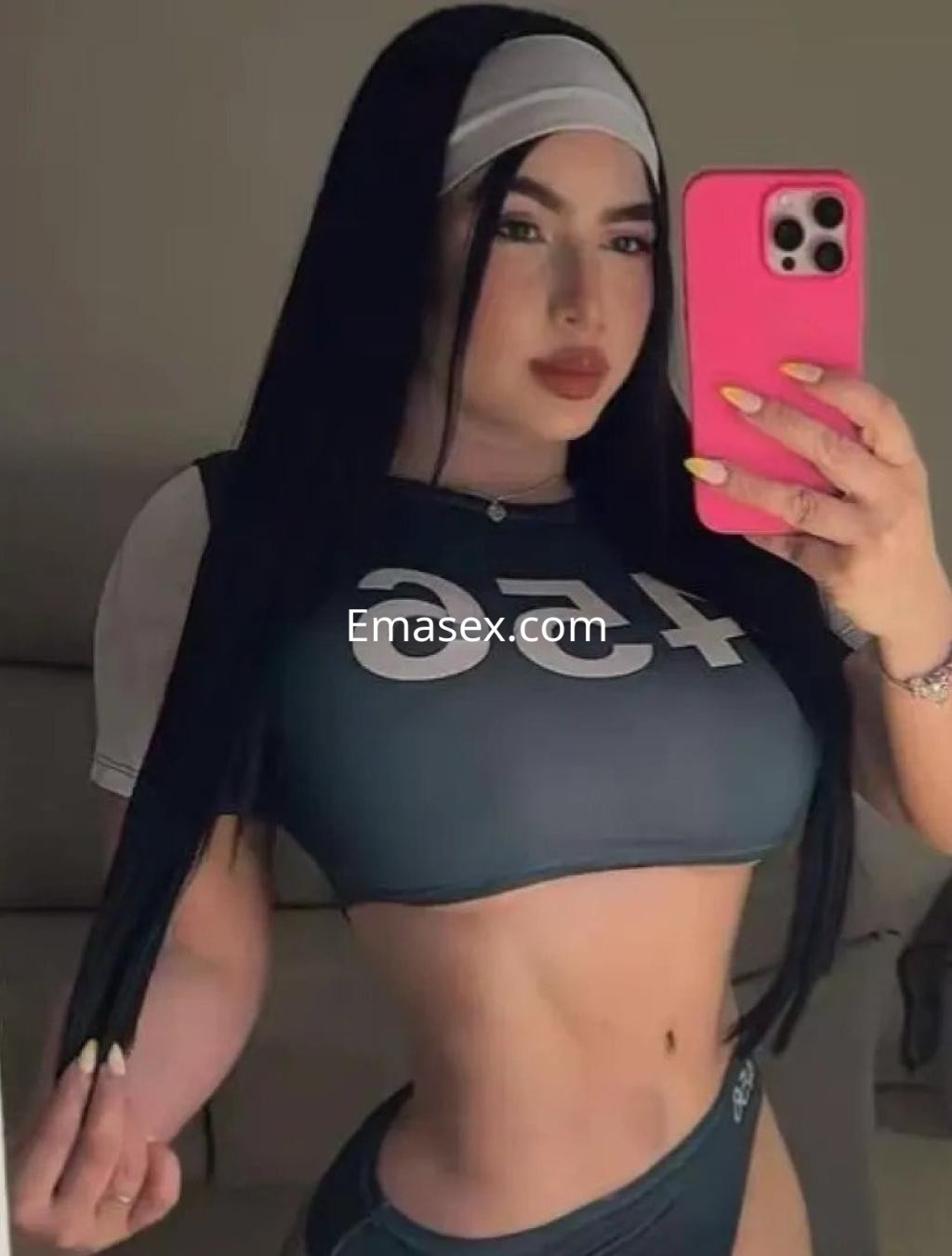 Escort en Córdoba con cabello largo y lacio, vistiendo un conjunto deportivo ajustado y sosteniendo un móvil.