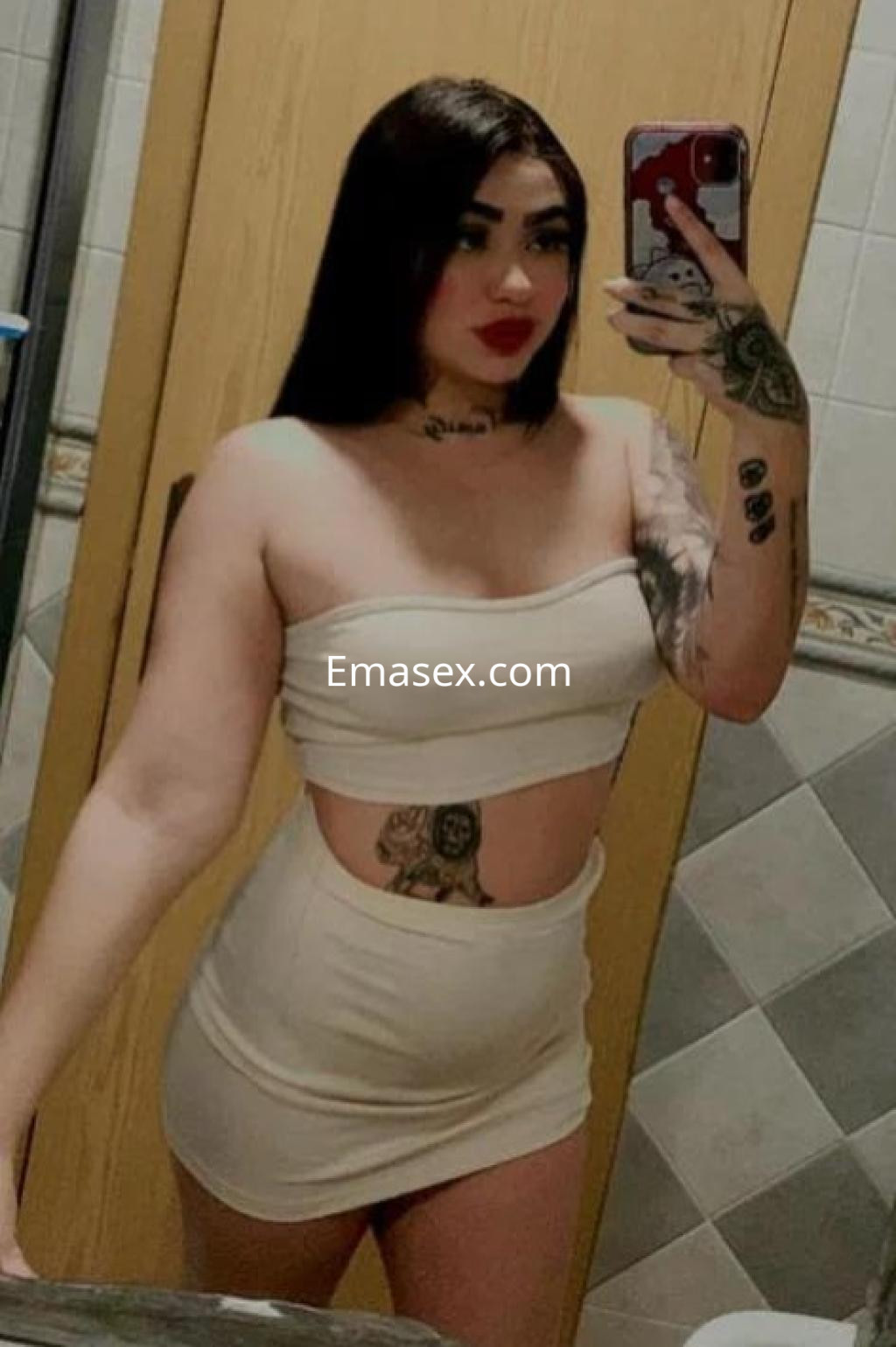 Puta con vestido ajustado color nude, tatuajes visibles y cabello largo, posando frente a un espejo en Castellón.
