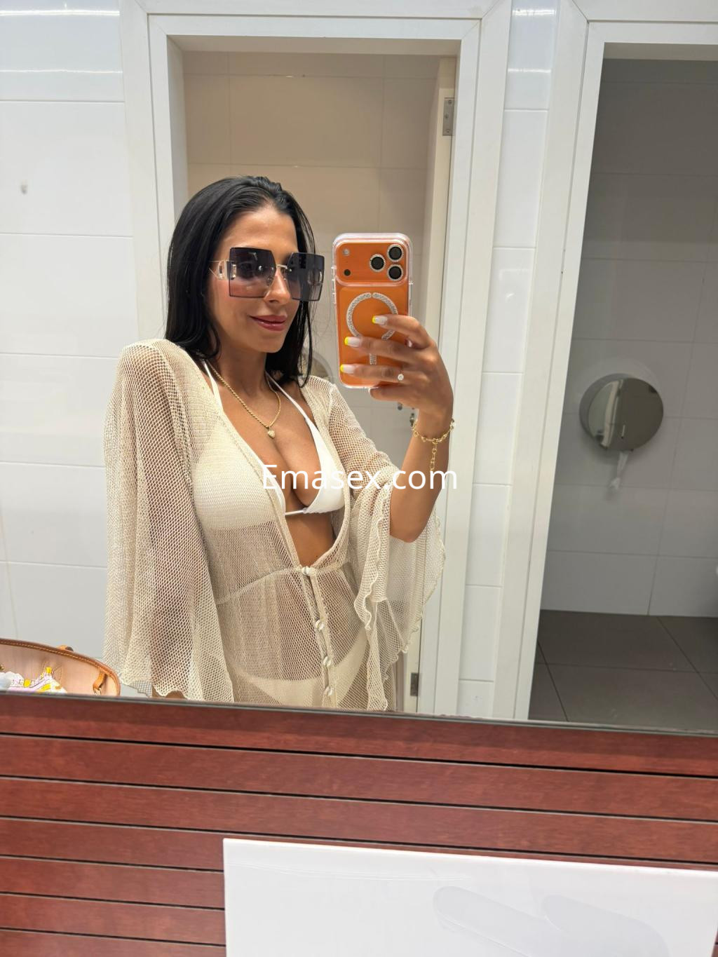 Escort en Donosti, luciendo un bikini blanco con una cubierta de red, posando frente al espejo con gafas de sol.