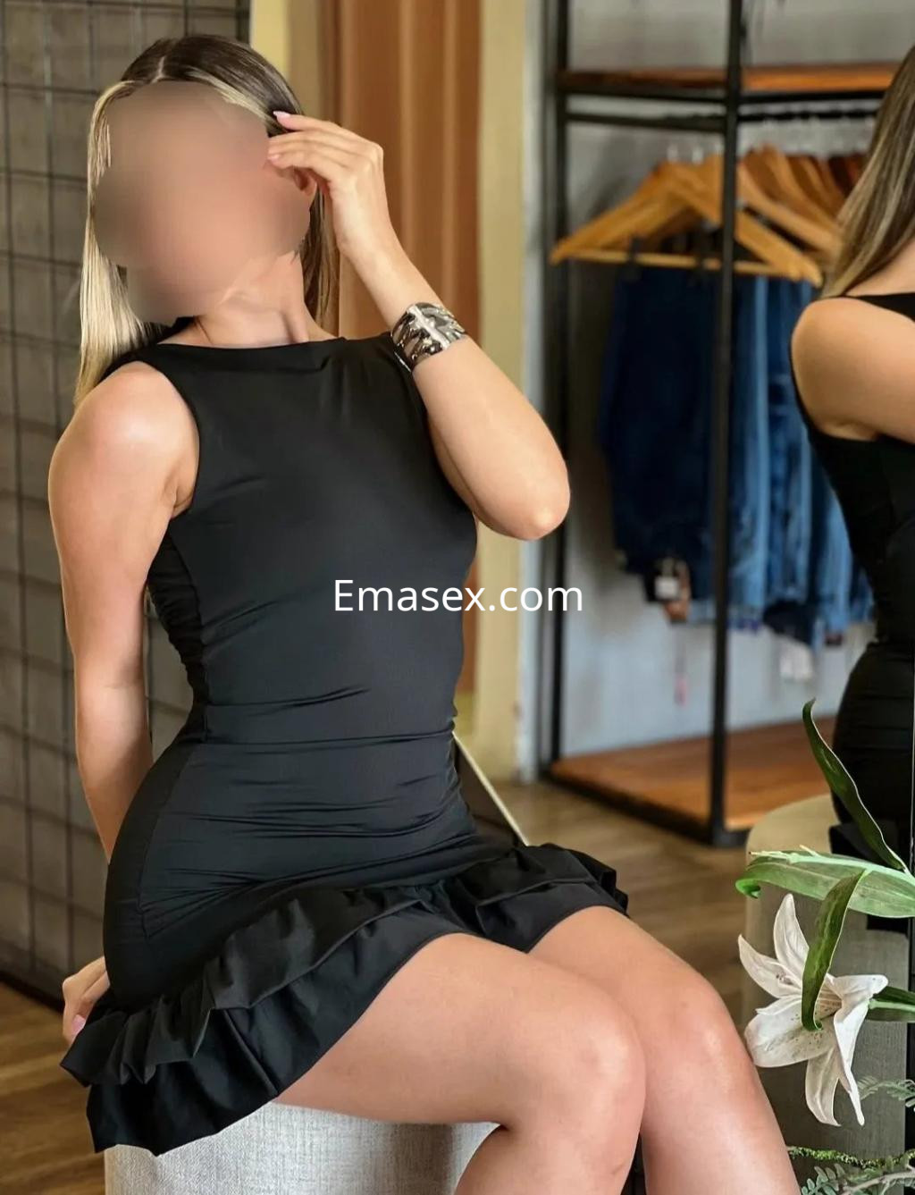 Puta en Albacete viste un vestido negro ajustado con volantes, posando sentada en un entorno elegante.