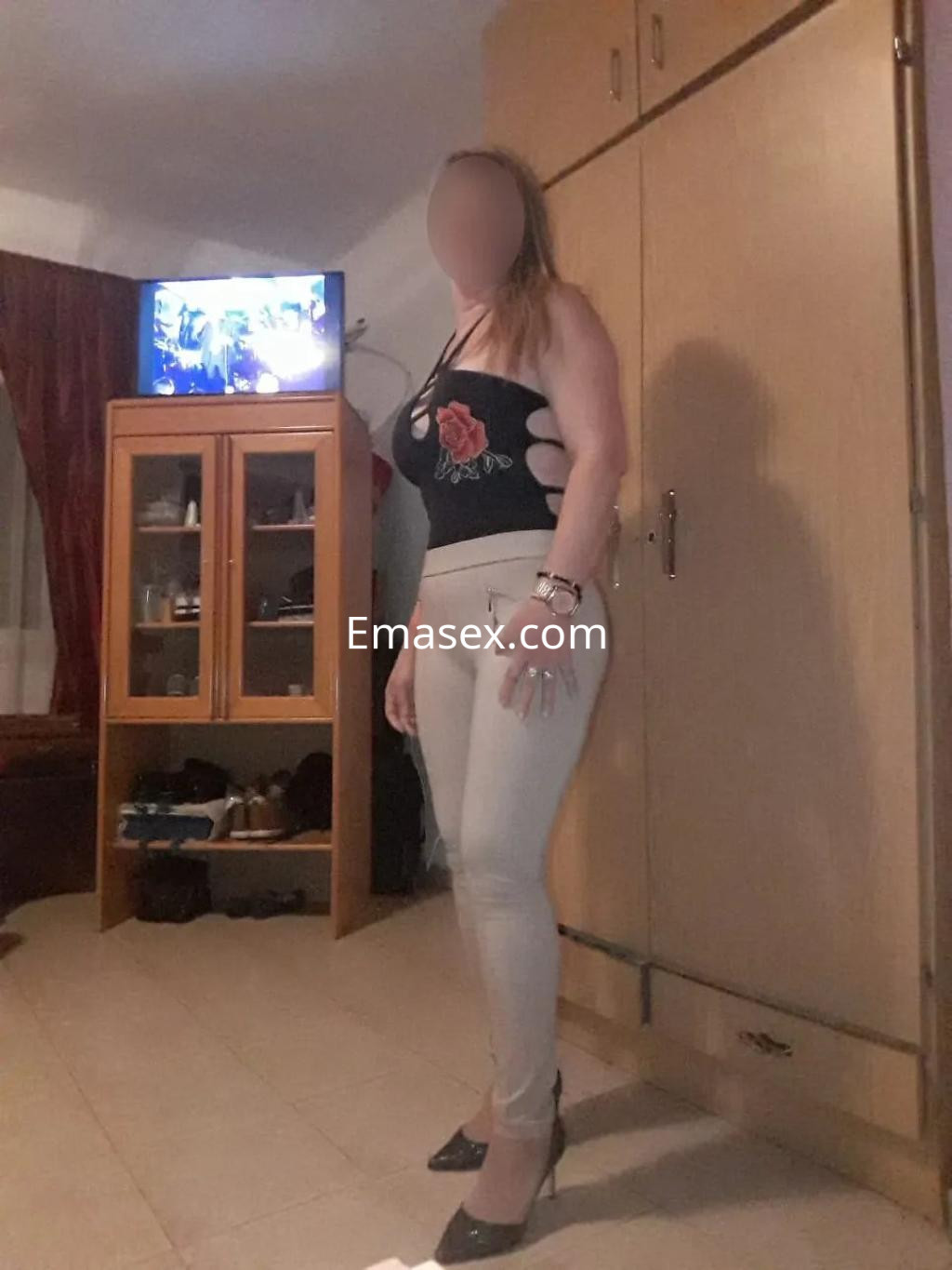 Escort en Albacete viste una blusa negra con detalles y jeans ajustados, posando en un ambiente interior.