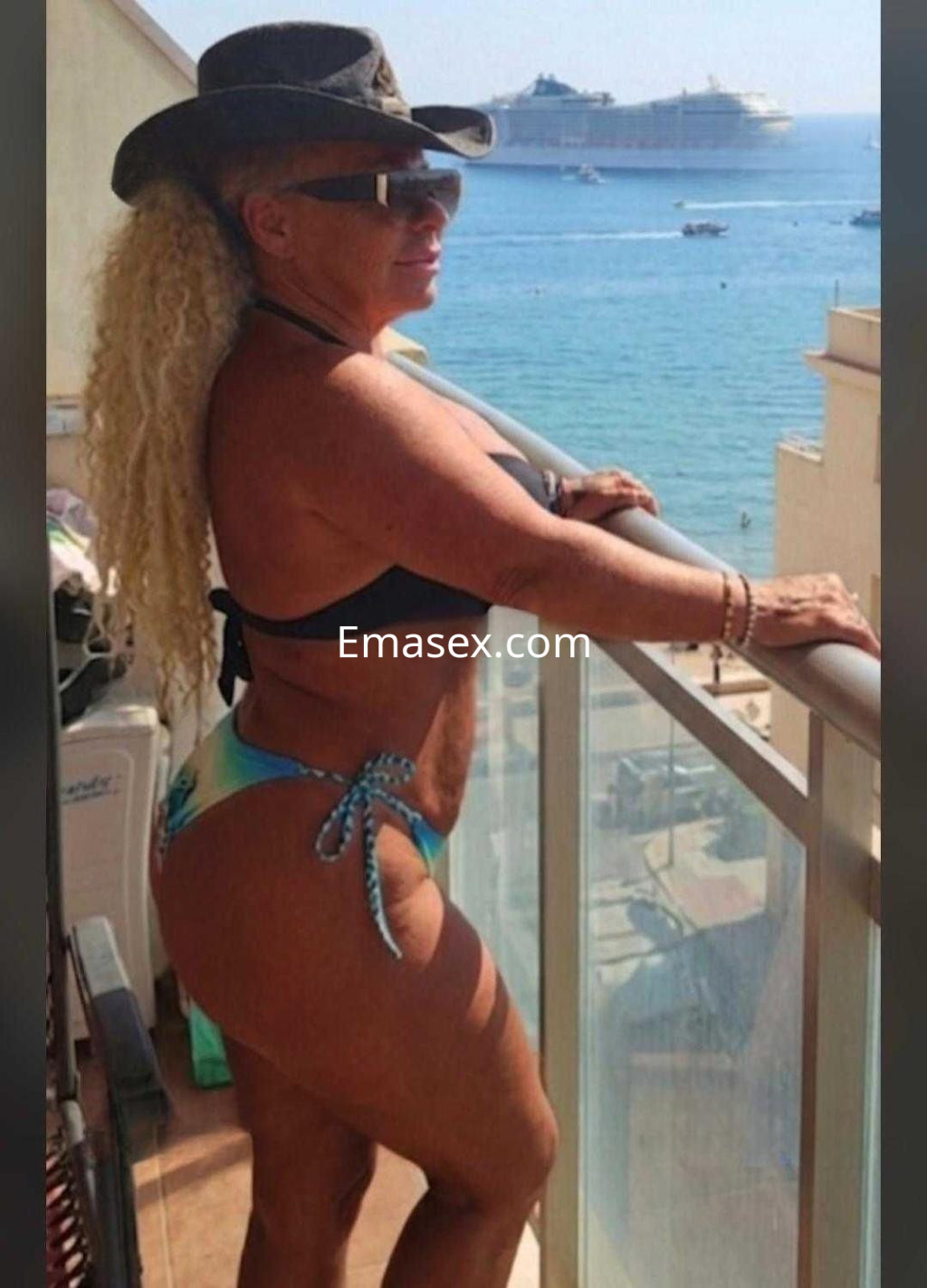 Escort en Alicante luciendo un bikini de colores claros y un sombrero, disfrutando de la vista al mar.