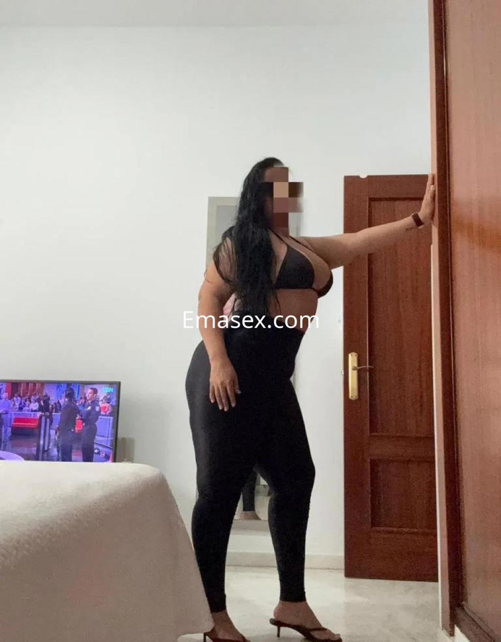 Puta de Badajoz luciendo un top negro y leggings ajustados, posando junto a una puerta en un ambiente interior.