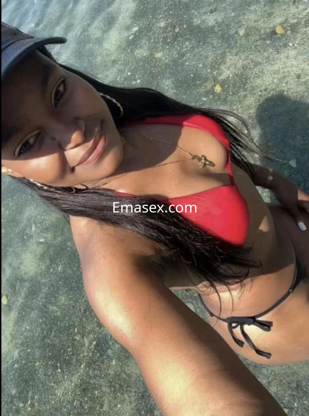 La puta en Badajoz luce un bikini rojo mientras sonríe en un entorno acuático con luz natural.