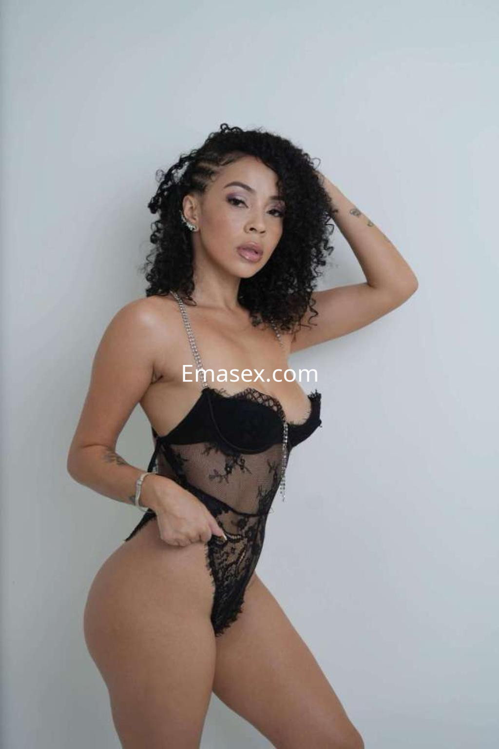 La escort en Ibiza posa con un body negro semitransparente, mostrando su cabello rizado y una actitud segura.