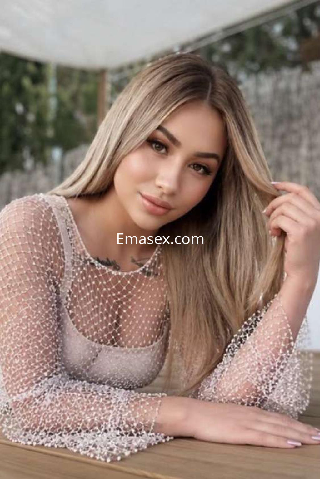 Puta con cabello largo y rubio, viste un top de malla transparente y posa en un entorno exterior en Ibiza.