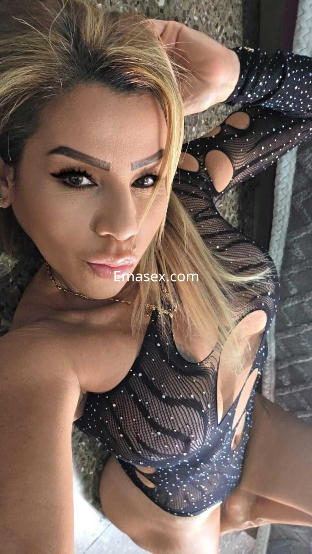 Escort con cabello rubio, viste un body negro con detalles cut-out y lentejuelas, posando en Barcelona.