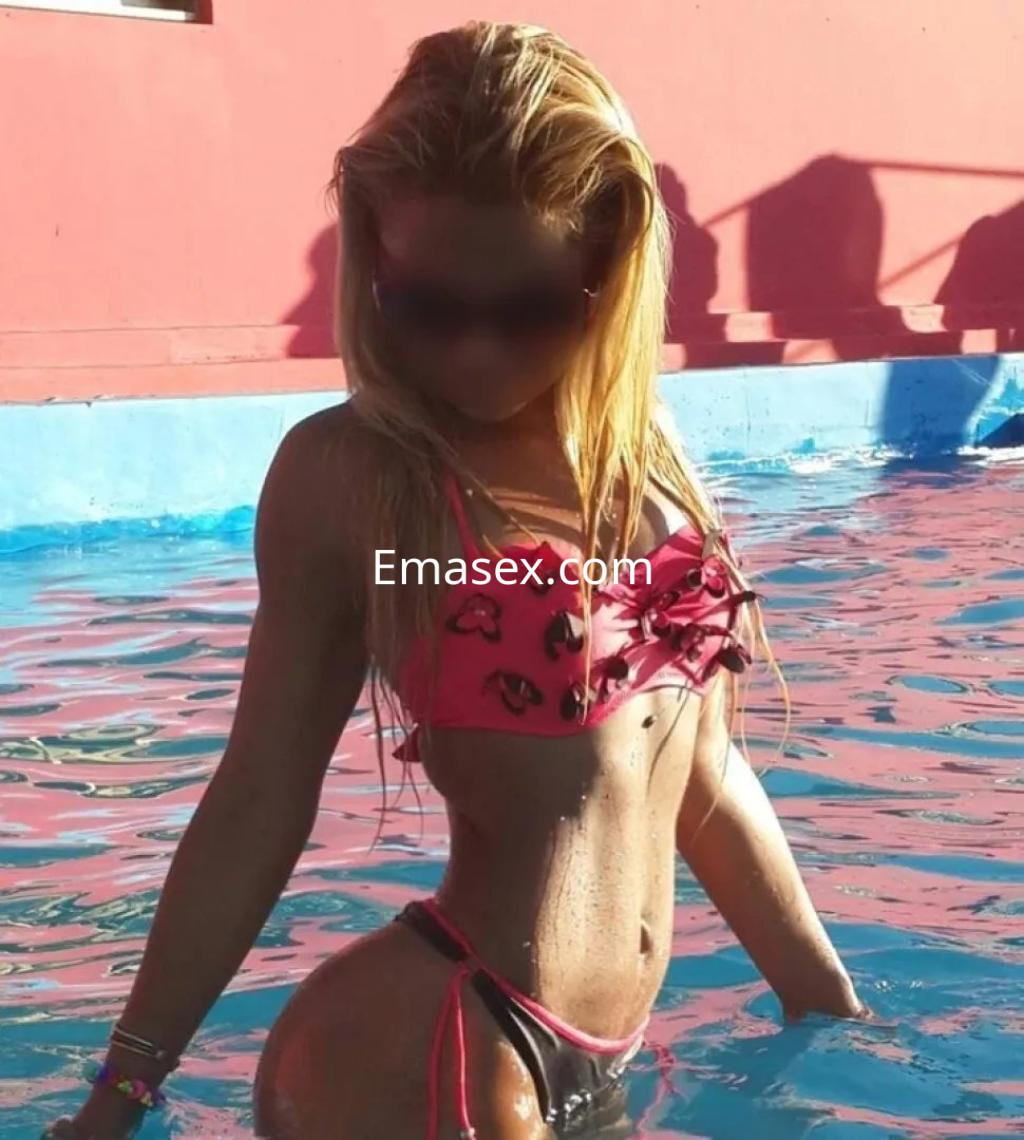 Puta en Barcelona posando junto a una piscina, con un bikini rosa que destaca su figura y cabello rubio largo.