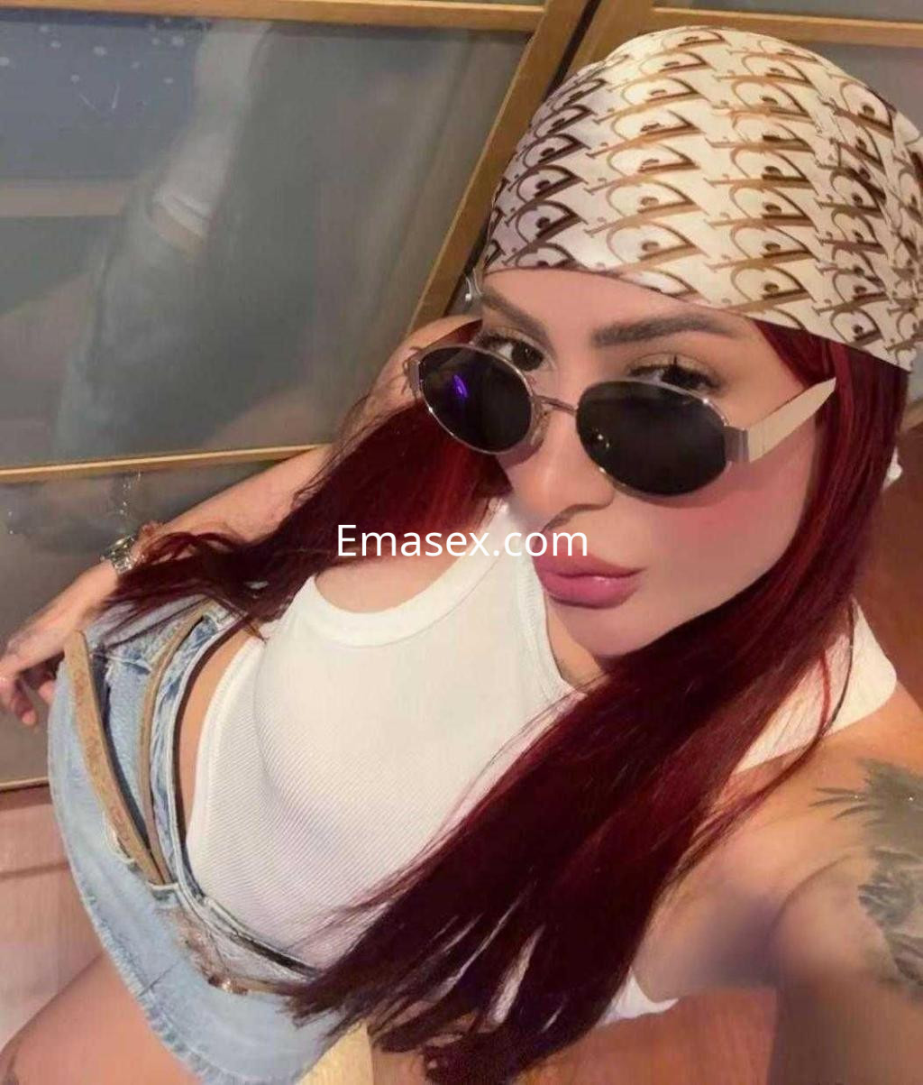 Puta en Barcelona con cabello rojo, usando gafas de sol y una blusa blanca ajustada con pantalones cortos de mezclilla.