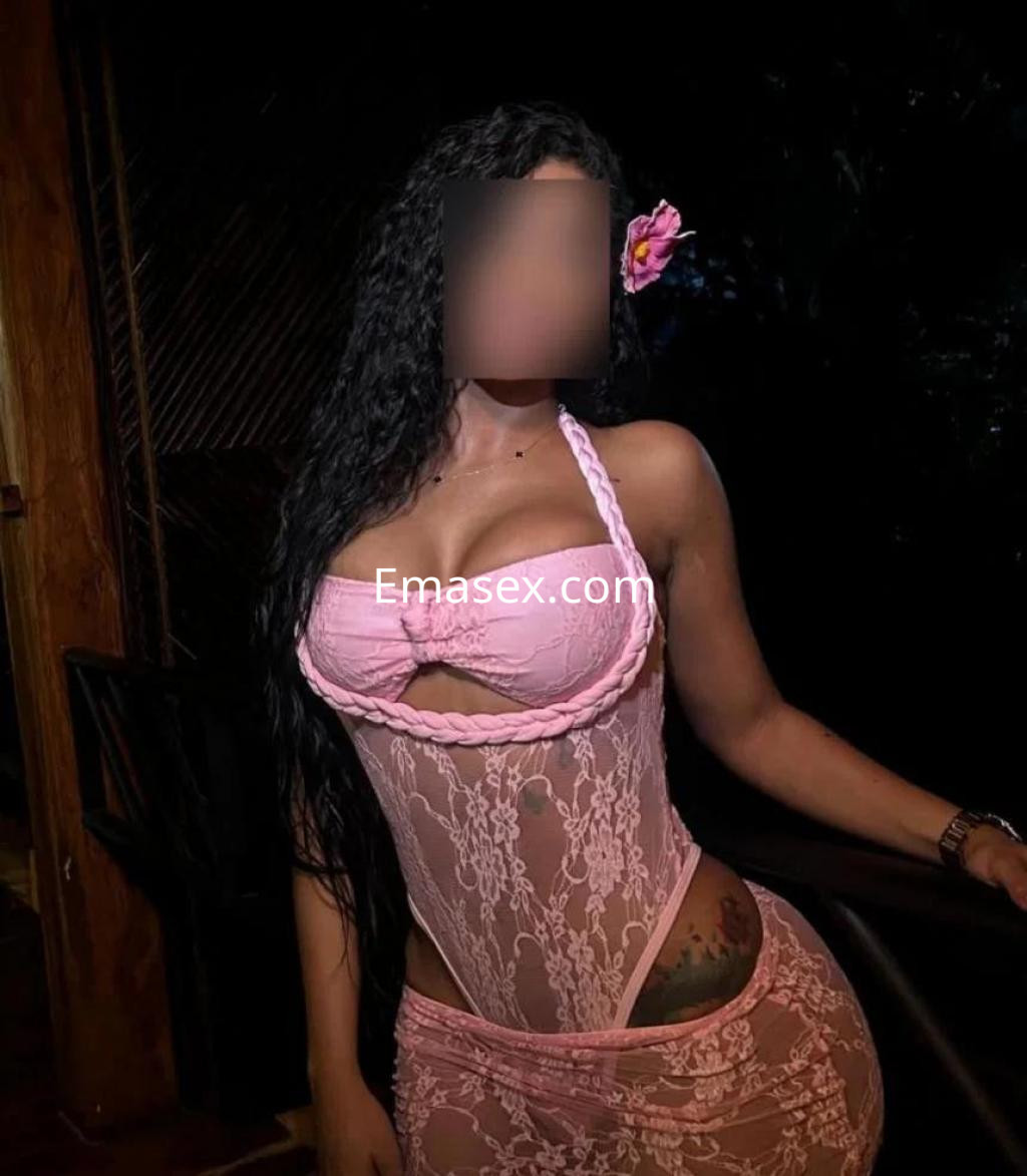 Escort en Barcelona con cabello rizado y largo, luciendo un vestido de encaje rosa que resalta su figura.