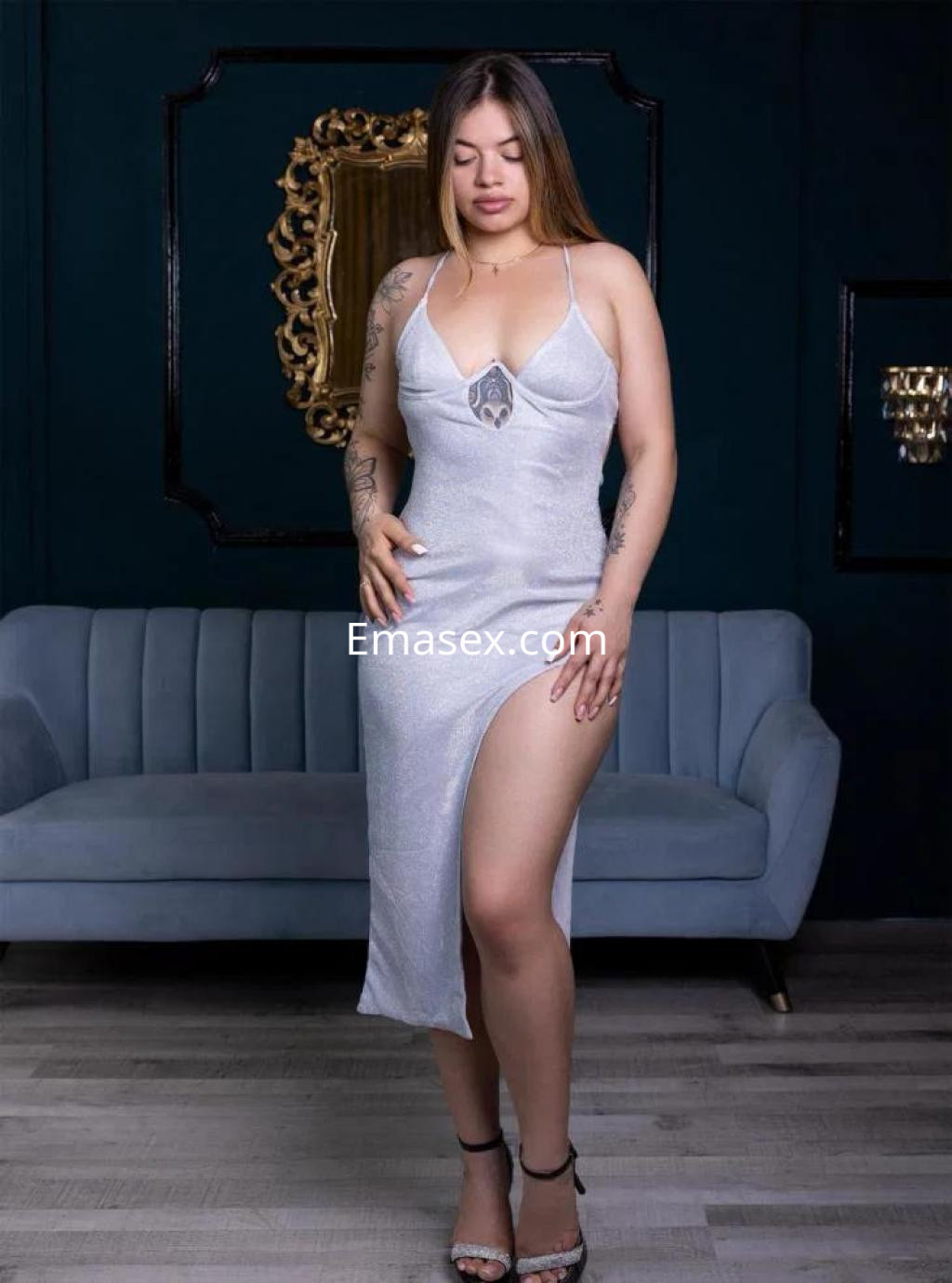 Escort en Barcelona con vestido plateado ajustado y abertura lateral, posando en un ambiente elegante.