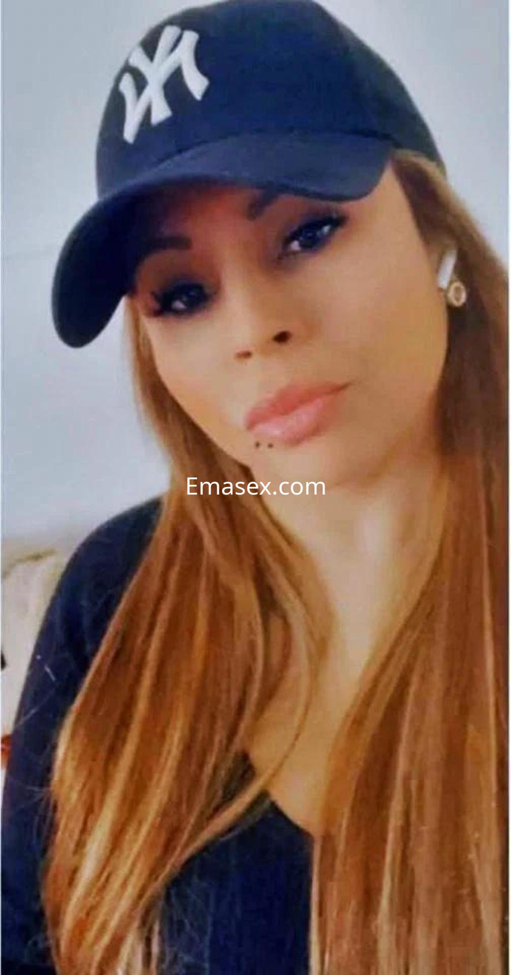 Escort en Barcelona con cabello largo y lacio, luciendo una gorra y un top negro, posando con una expresión serena.