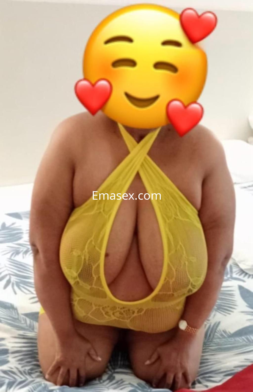 Puta en Barcelona viste un atrevido conjunto de lencería amarilla, posando de rodillas en una cama.