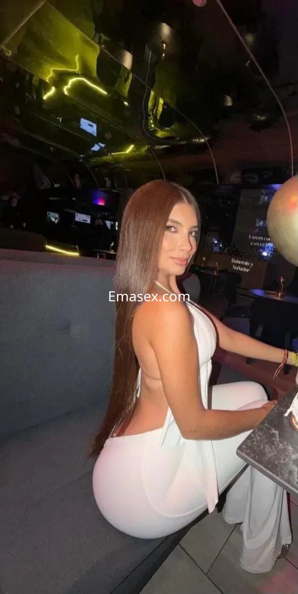 Puta posando en un ambiente elegante de Burgos, con un vestido blanco ajustado que resalta su figura y cabello largo.
